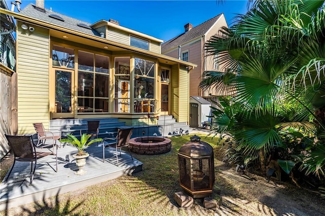 back of property featuring a wooden deck, a fire pit, and a sunroom