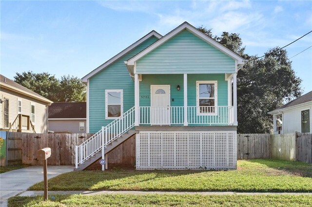 view of front of property featuring a front lawn, a porch, fence, and stairs