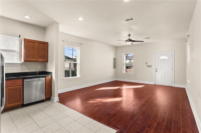 kitchen with light wood-style flooring, stainless steel dishwasher, visible vents, brown cabinets, and dark countertops