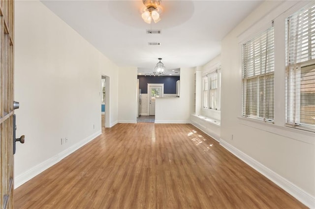 unfurnished living room with hardwood / wood-style flooring, plenty of natural light, and ceiling fan with notable chandelier