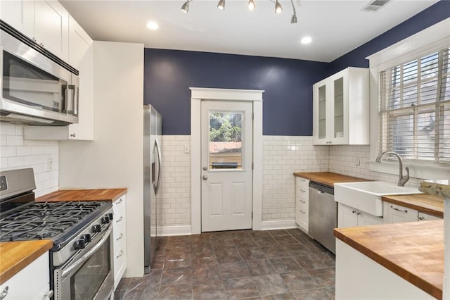 kitchen with appliances with stainless steel finishes, white cabinetry, and butcher block counters