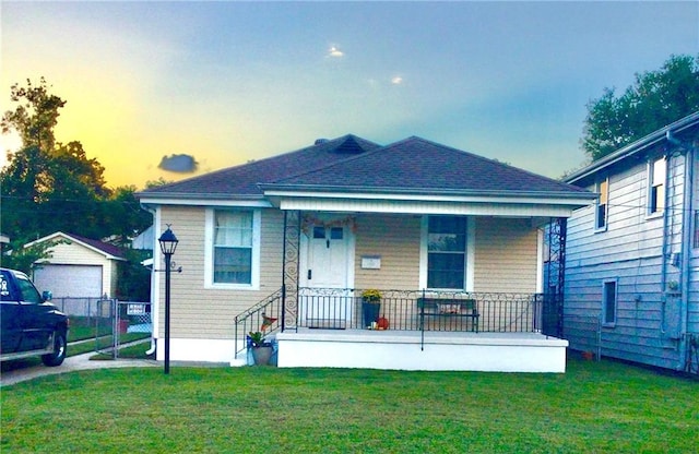 bungalow with covered porch, a garage, an outbuilding, and a lawn