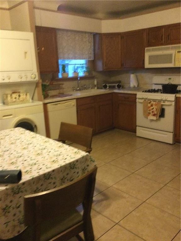 kitchen featuring stacked washing maching and dryer, tasteful backsplash, light tile patterned floors, and white appliances