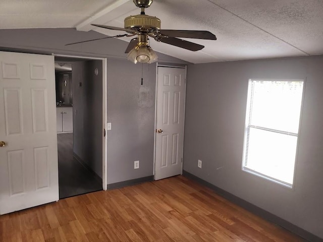 unfurnished bedroom with vaulted ceiling with beams, multiple windows, hardwood / wood-style floors, and ceiling fan