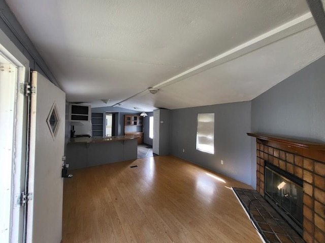 unfurnished living room featuring a textured ceiling, vaulted ceiling, a fireplace, and wood-type flooring