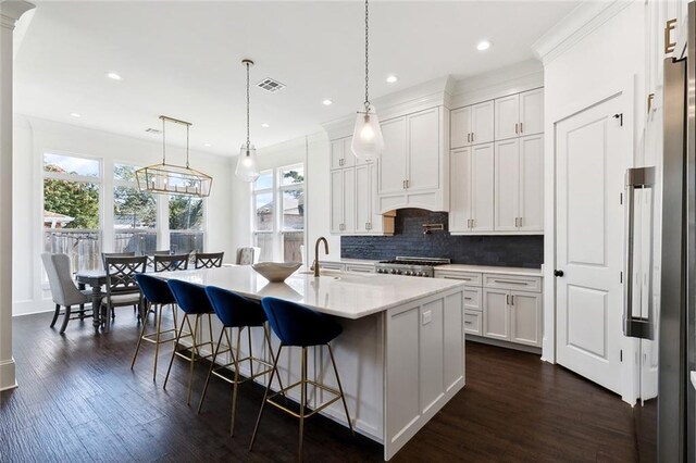 kitchen featuring decorative light fixtures, a center island with sink, white cabinets, decorative backsplash, and stove