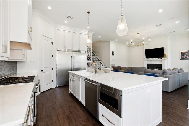 kitchen with appliances with stainless steel finishes, hanging light fixtures, white cabinetry, dark wood-type flooring, and a center island with sink