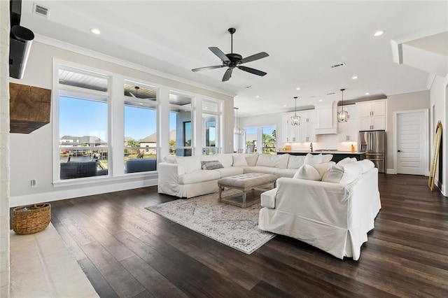 living room with sink, a water view, ornamental molding, dark hardwood / wood-style flooring, and ceiling fan with notable chandelier