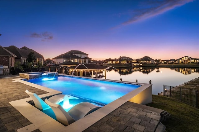 pool at dusk featuring a water view, pool water feature, and an in ground hot tub