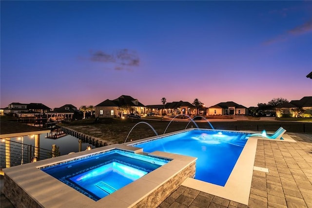 pool at dusk featuring an in ground hot tub and a patio area