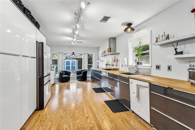 kitchen featuring wall chimney range hood, light hardwood / wood-style flooring, sink, white cabinets, and appliances with stainless steel finishes