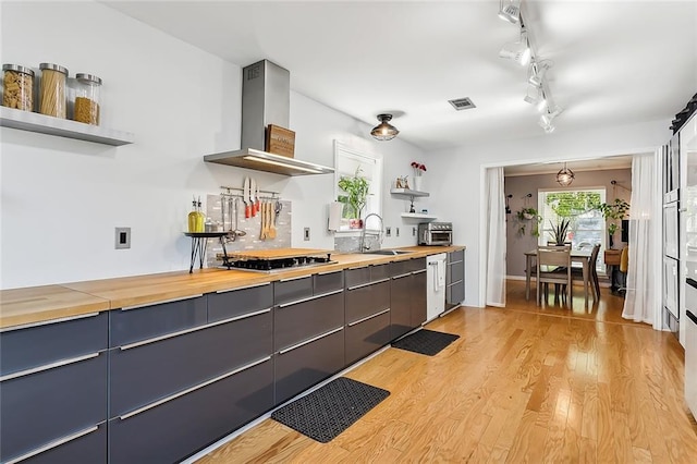 kitchen with sink, light hardwood / wood-style floors, wall chimney exhaust hood, wooden counters, and stainless steel gas stovetop