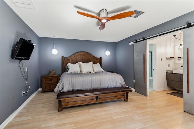 bedroom featuring light hardwood / wood-style flooring, a barn door, ensuite bathroom, and ceiling fan