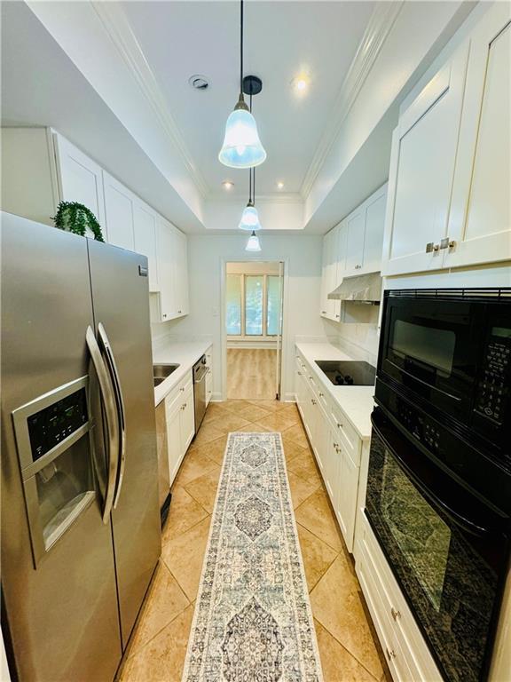 kitchen with white cabinets, a raised ceiling, ornamental molding, decorative light fixtures, and black appliances