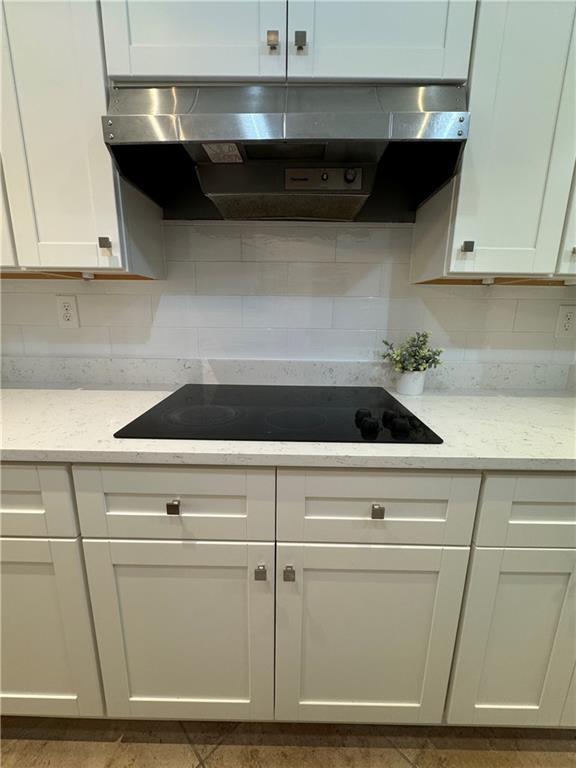 kitchen featuring black electric stovetop, backsplash, exhaust hood, and white cabinetry