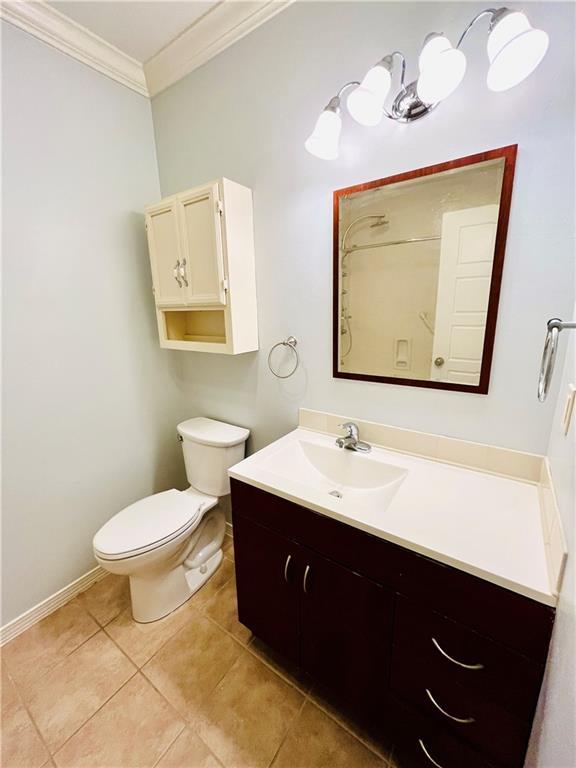 half bath featuring tile patterned flooring, toilet, vanity, baseboards, and ornamental molding