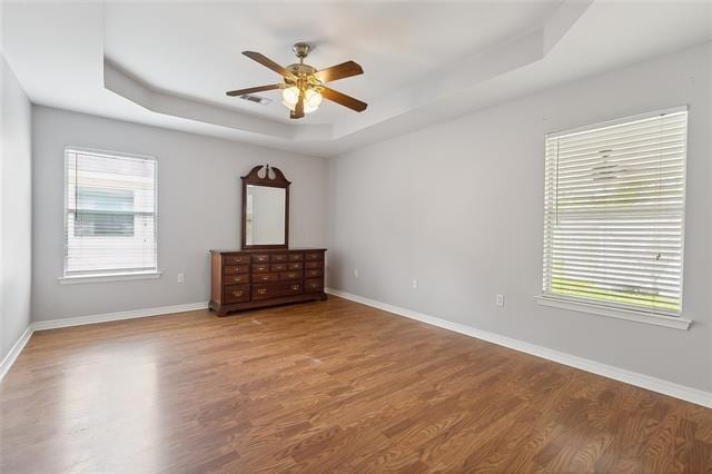 unfurnished bedroom with multiple windows, wood-type flooring, ceiling fan, and a raised ceiling