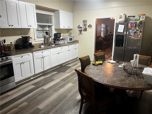 kitchen with white cabinetry, appliances with stainless steel finishes, wood-type flooring, and dark stone countertops