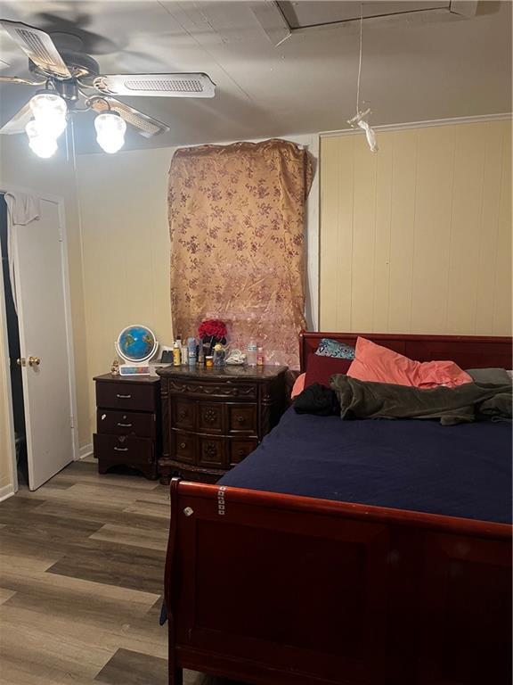 bedroom featuring wood walls, hardwood / wood-style flooring, and ceiling fan