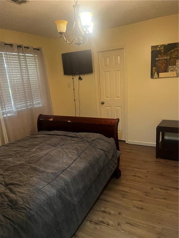 bedroom with dark hardwood / wood-style flooring, a textured ceiling, and a chandelier