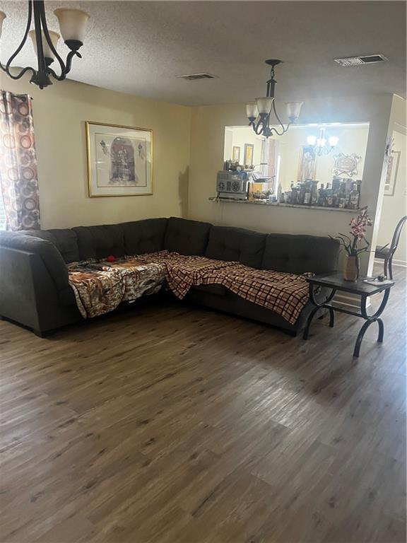 living room featuring dark wood-type flooring, a textured ceiling, and a notable chandelier