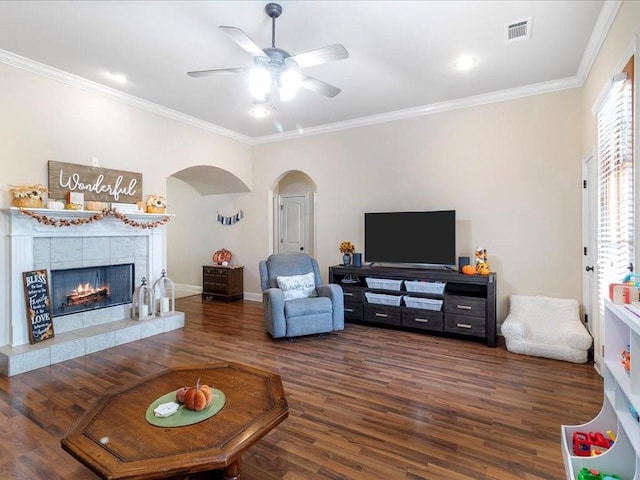 living room featuring crown molding, dark hardwood / wood-style floors, a tile fireplace, and ceiling fan