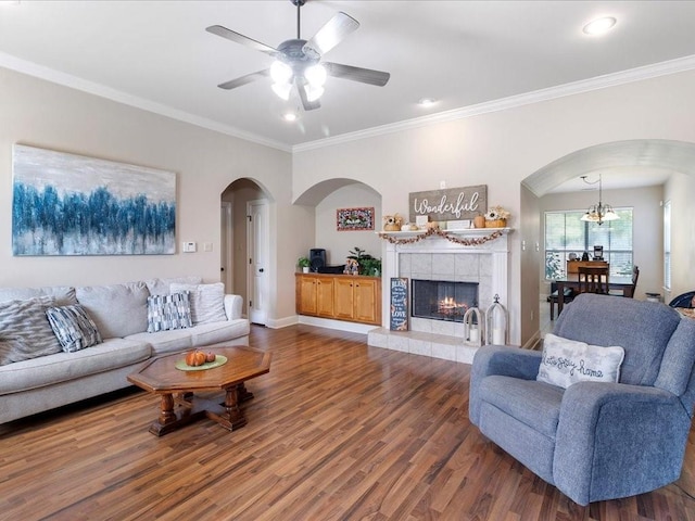 living room featuring crown molding, hardwood / wood-style flooring, ceiling fan with notable chandelier, and a fireplace