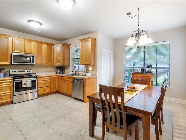 kitchen featuring light tile patterned floors, appliances with stainless steel finishes, pendant lighting, a notable chandelier, and sink