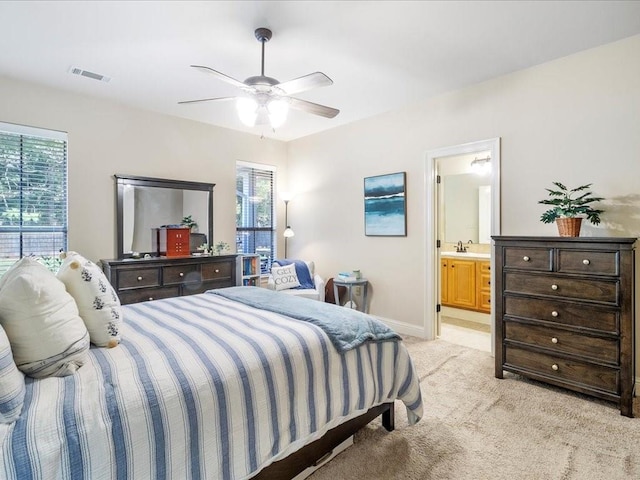 bedroom featuring ensuite bathroom, light carpet, multiple windows, and ceiling fan