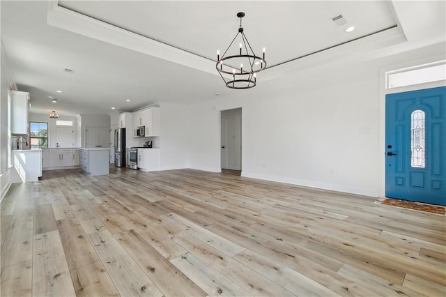 unfurnished living room featuring a raised ceiling, light hardwood / wood-style floors, and an inviting chandelier