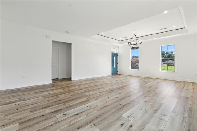 spare room with a tray ceiling, light hardwood / wood-style floors, and a notable chandelier