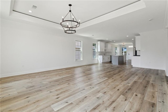 unfurnished living room with a raised ceiling, an inviting chandelier, light hardwood / wood-style flooring, and crown molding