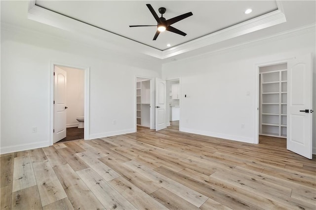 unfurnished bedroom with a tray ceiling, a spacious closet, ceiling fan, and ensuite bathroom