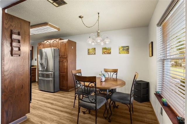 dining space with a notable chandelier, a textured ceiling, and light wood-type flooring