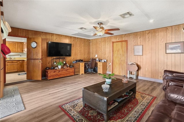 living room with light hardwood / wood-style flooring, wood walls, and ceiling fan