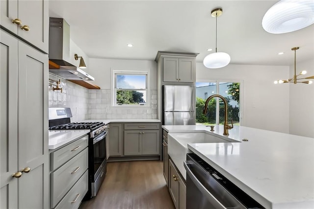 kitchen with a wealth of natural light, sink, wall chimney range hood, and appliances with stainless steel finishes