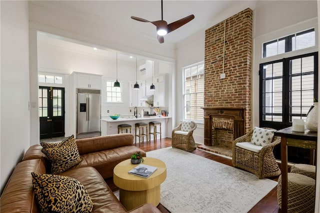 living room with ceiling fan, wood-type flooring, a brick fireplace, a high ceiling, and french doors