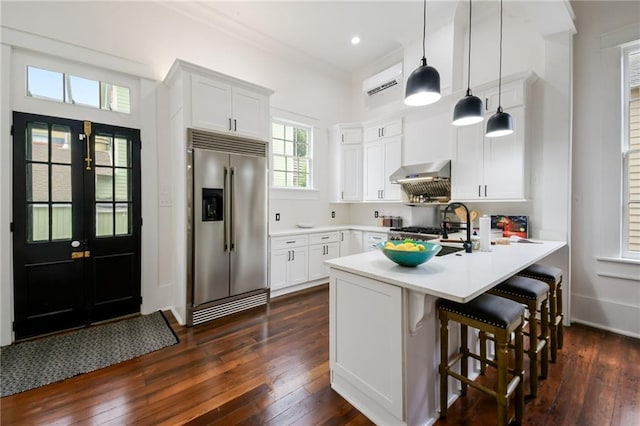 kitchen featuring stainless steel built in fridge, a breakfast bar, decorative light fixtures, white cabinets, and dark hardwood / wood-style flooring