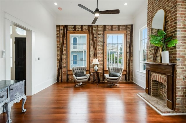 unfurnished room featuring wood-type flooring, a fireplace, ceiling fan, brick wall, and ornamental molding