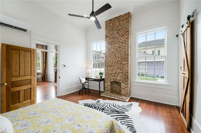 bedroom featuring a wall mounted AC, dark hardwood / wood-style flooring, ceiling fan, a barn door, and crown molding