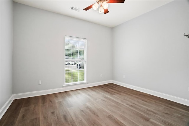 empty room featuring a ceiling fan, baseboards, visible vents, and wood finished floors