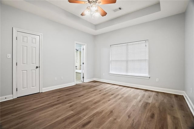 spare room with a ceiling fan, visible vents, baseboards, a raised ceiling, and dark wood-style floors