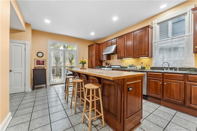 kitchen with a kitchen island, appliances with stainless steel finishes, light tile patterned flooring, sink, and butcher block countertops