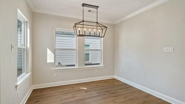 unfurnished dining area featuring dark wood-type flooring, crown molding, and a notable chandelier