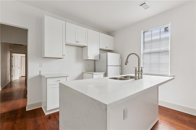 kitchen with a kitchen island with sink, sink, white cabinets, white fridge, and dark hardwood / wood-style flooring