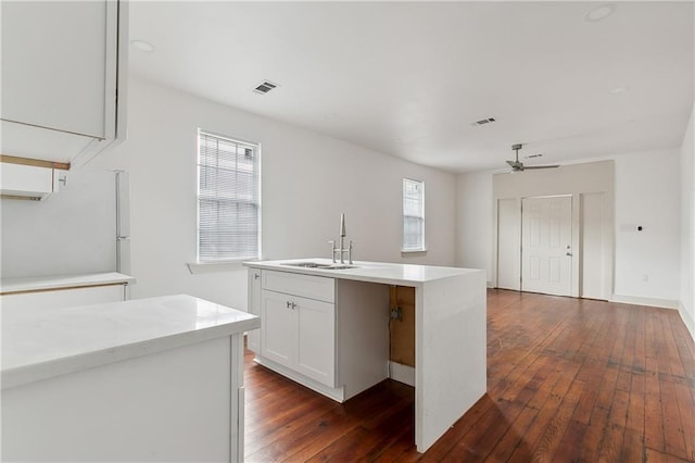 kitchen with white cabinets, dark wood-type flooring, plenty of natural light, and an island with sink