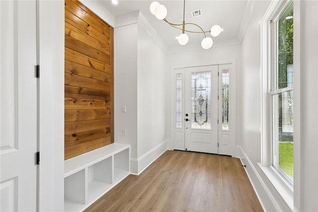 entryway featuring wooden walls, ornamental molding, light wood-type flooring, and a notable chandelier