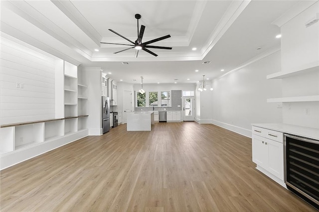 unfurnished living room with ceiling fan with notable chandelier, a raised ceiling, wine cooler, built in features, and ornamental molding