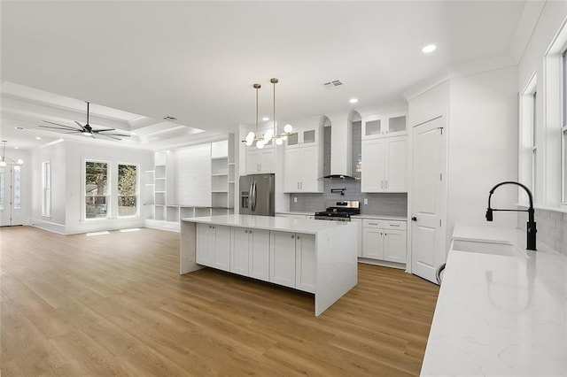 kitchen featuring white cabinetry, sink, wall chimney range hood, pendant lighting, and appliances with stainless steel finishes