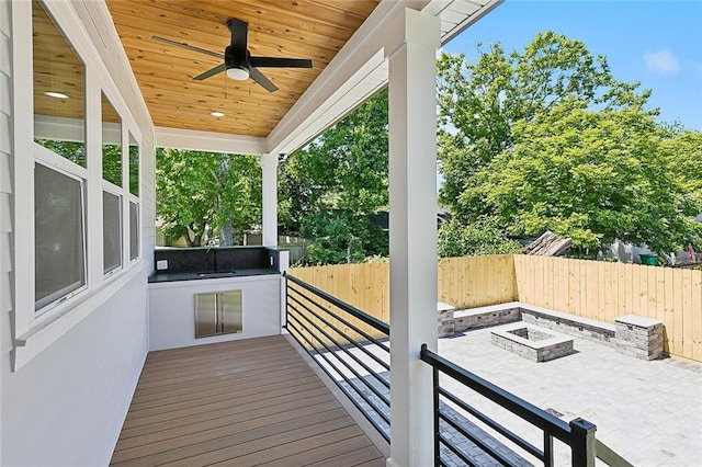 deck with ceiling fan, sink, an outdoor kitchen, an outdoor fire pit, and a patio area